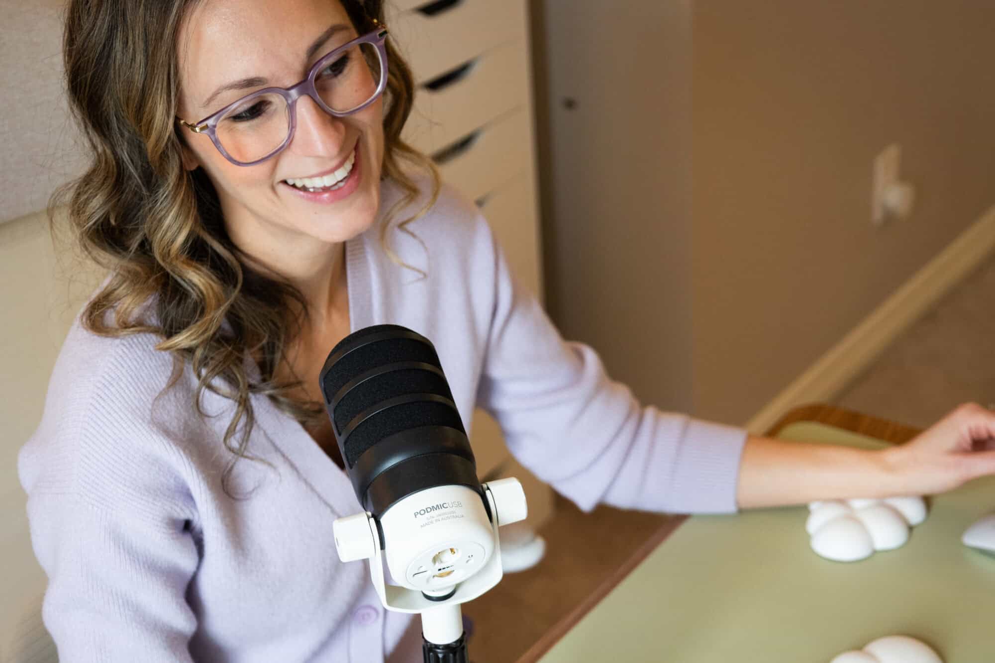 Melissa Choquette sits at a desk speaking into a microphone while looking toward a computer screen, representing virtual conversation and online community connection.
